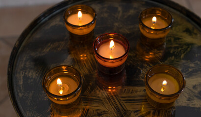 Fünf brennende Opferkerzen in Glasschalen auf einem dunklen runden Tablett in Nahaufnahme