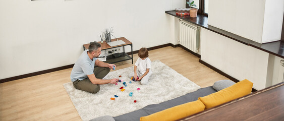 Dad and son play with construction set on carpet