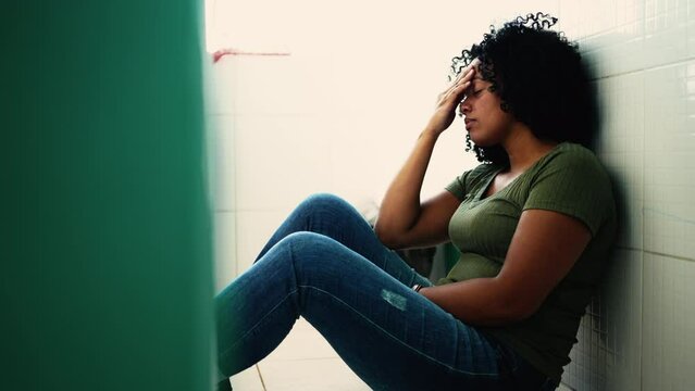 Stressed African American young woman suffering from depression. A black hispanic latin adult girl seated on kitchen floorin mental distress