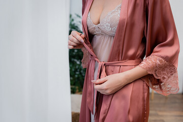 Cropped view of woman in nightie tying silk robe at home.