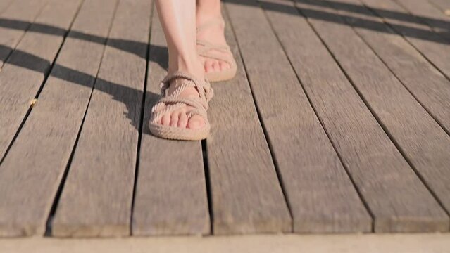 Female legs in natural woven sandals walk on wooden floor and on green lawn grass in park. Enjoying nature, life, freedom concept. Healthy lifestyle. Close-up of bare feet and grass. Slow motion 