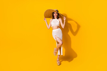 Fototapeta na wymiar Full length photo of carefree shiny lady wear white outfit arms hands hat walking isolated yellow color background