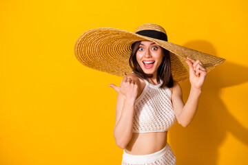 Photo of excited funky girl dressed knitted look sunhat open mouth pointing thumb back empty space isolated yellow color background