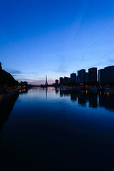 View along the River Seine to the Eiffel tower, the river embankment, and the city at dusk, reflections on the water.