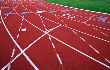 A red artificial surface running track. A sports ground. Painted marked lines for lanes.