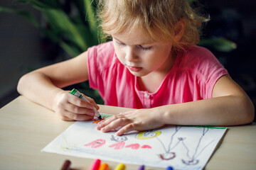 Little girl drawing a picture with colored markers, sitting at the table