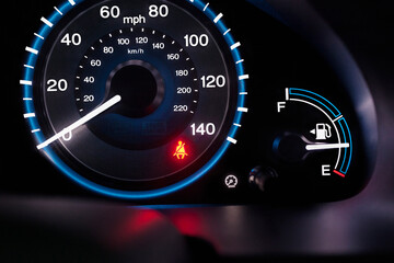 A lit up car dashboard, mph speed dial, in miles and kilometres, fuel guard and a red warning seatbelt light.