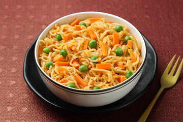 Schezwan Noodles or vegetable Hakka Noodles or chow mein, served in a bowl or plate with tomato sauce, ketchup, wooden chopsticks, India. popular Indo-Chinese Indian Maggi noodles.