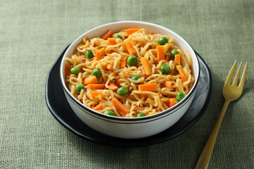 Schezwan Noodles or vegetable Hakka Noodles or chow mein, served in a bowl or plate with tomato sauce, ketchup, wooden chopsticks, India. popular Indo-Chinese Indian Maggi noodles.