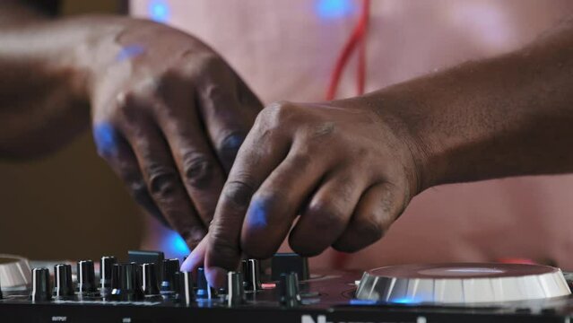 Unrecognizable unknown cool African DJ standing at mixer controller composing new sound song audio mix and rocking party in nightclub enjoying nightlife play electronic music rotates volume buttons