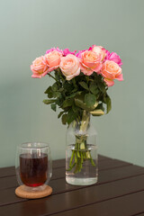 Bouquet of roses with glass of tea on a wooden table on a green background.