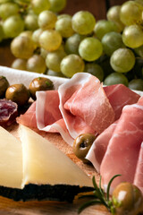 Tagliere con tipici salumi, prosciutti, olive, uva fresca e formaggi - cibo italiano 