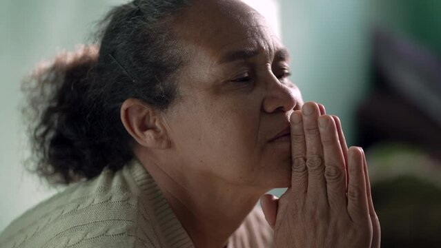 Older woman praying to God at home. One hispanic senior lady in prayer closeup face. Hispanic South American person