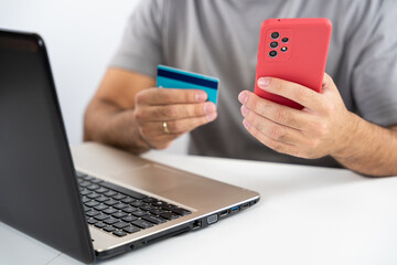 Unrecognizable young man with computer and holding card and cell phone to shop online from home - concept shopping, black friday, cyber monday, sales, christmas