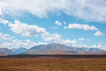 Motley autumn landscape with sunlit high mountain plateau and beautiful mountain top under dramatic cloudy sky. Vivid autumn colors in mountains. Sunlight and shadows of clouds in changeable weather.