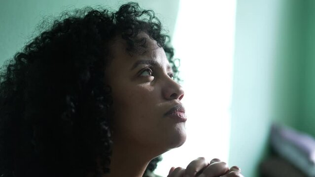 A spiritual African Woman opening eyes to sky in prayer having HOPE during hard times. A faithful hispanic girl looking up