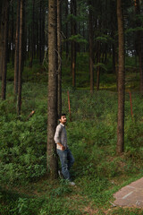 Guy standing leaning against tree. Beautiful green himalayan cedar tree forest