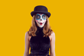 Wondering amazed teen girl in black halloween costume and hat with scary makeup on yellow...