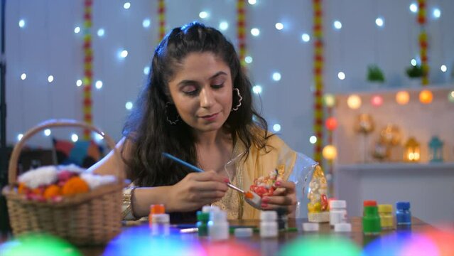 A beautiful Indian girl in an ethnic dress painting a Hindu God idol - Indian culture and customs. Indian young female doing preparation for Diwali puja celebrations - Colorful decorated background...