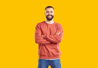 Young smiling bearded man wearing in red sweatshirt and jeans posing with arms crossed on chest on...