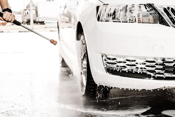 A man's hand washes his white car at the sink. Soap suds on a car