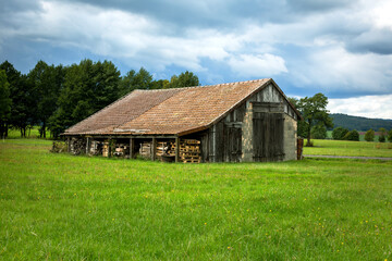 Plakat barn in the middle of a green field and cloudy sky