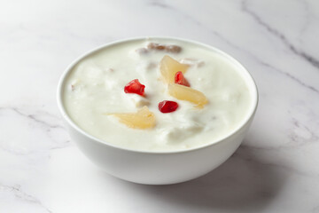 Close-up of Fruits raita or Yogurt & Pineapple or Ananas Raita garnished with pineapple piece and pomegranate, served in a white ceramic bowl over whiet granite background