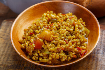 Spelled with vegetables stewed in a wooden plate on a handmade wooden board.
