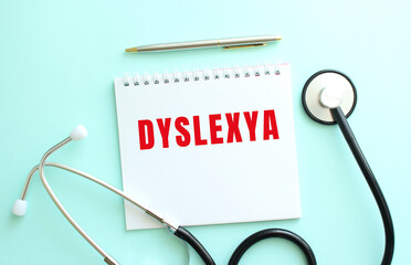 White notepad with red text DYSLEXYA and stethoscope on a blue background.