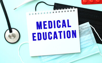 The blue text MEDICAL EDUCATION is written in a notebook that lies on a blue background next to a medical masks