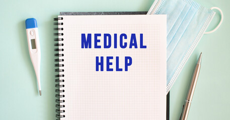 Notepad, medical mask, thermometer and pen on a blue background. MEDICAL HELP text in a notebook.