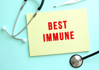 The text BEST IMMUNE is written in a yellow pad that lies next to the stethoscope on a blue background.