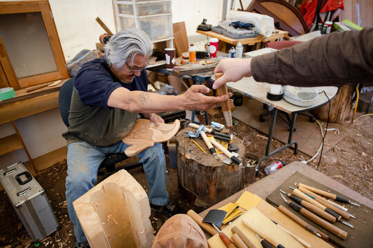 Male Indigenous woodworker reaching for tool from coworker in workshop