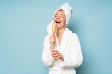 Portrait of woman in bathrobe and towel on head with closed eyes singing in massage brush
