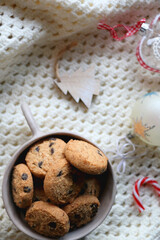 Fototapeta na wymiar Bowl of cookies, soft knitted blanket and colorful Christmas ornaments at home. Flat lay.