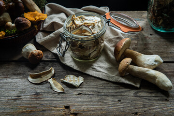 Glass jar with dried porcini and fresh porcini on wooden table on dark background 