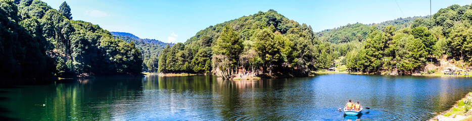 Fototapeta na wymiar panoramic of lake with boat in the water, green forest around and blue sky in dam of the llano, villa del carbon state of mexico 