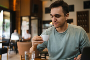 A young guy using his computer in cafe and talking on the phone while drinking water and coffee 
