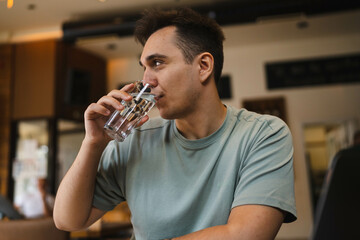 A young guy using his computer in cafe and talking on the phone while drinking water and coffee 