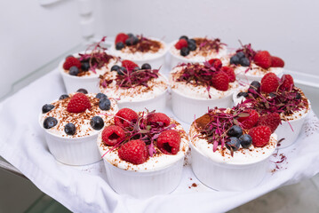 Desserts on a tray in the refrigerator. White ramekins with chilled desserts with berries. Raspberries, blueberries, cocoa powder.