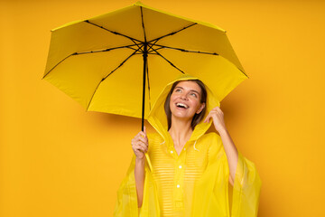Woman in waterproof rain coat standing under umbrella looking up with excitement