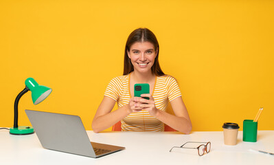 Office worker browsing social media on phone instead of working sitting at table in front of laptop