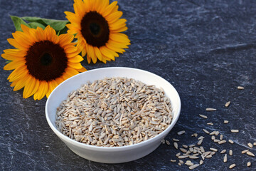 Sunflowers with a bowl of sunflower seeds on a dark background.