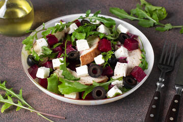 Salad with beetroot, chicken, feta cheese, arugula and black olives on brown background. Healthy food