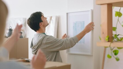 Home and painting for interior design after moving to new building, flat or apartment. Man, couple and art hanging on wall of lounge, happy together to decor in study, living room or office of house
