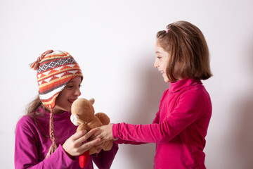 Little girl giving her teddy bear toy to older sister. Cute child girl giving a gift to her sister. Child girl sharing a toy with a friend