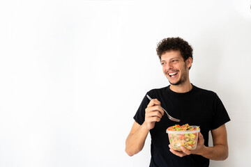 Happy young caucasian man eating and holding a healthy mediterranean pasta salad tupperware