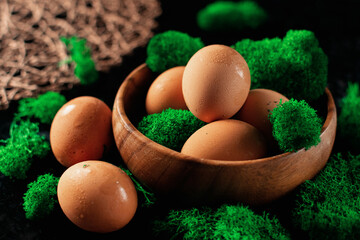 Chicken eggs in a wooden plate, there is a lot of natural green moss around, a homemade village product, fine water condensation on the eggs due to temperature changes