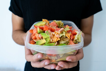 Hands holding a healthy mediterranean pasta salad tupperware