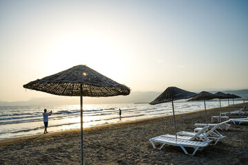 People walks and takes photo on beach at sunset, lounge chair, beach umbrella parasol, tanning bed